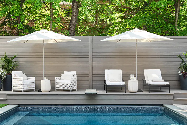 Front view of a backyard in-ground pool with a light gray deck and matching privacy wall.