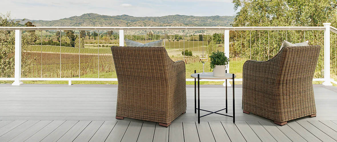 Gray deck with white railing and vertical cable rail infill looks out at mountains and farmland