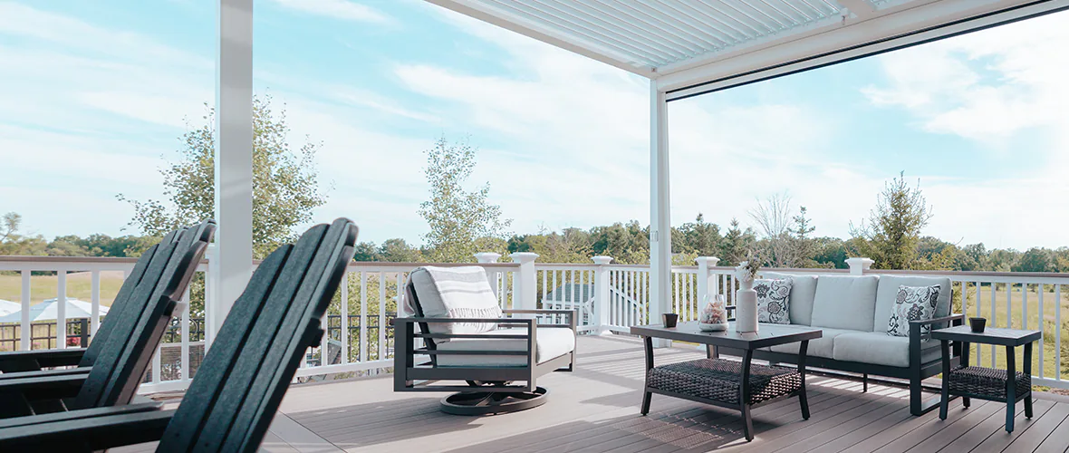 Light gray deck with multiple seating areas is partially shaded from the sun as it sits underneath a pergola