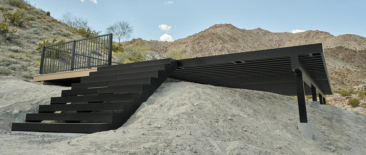 View of aluminum stairs that lead up to a substructure built into a desert hill.
