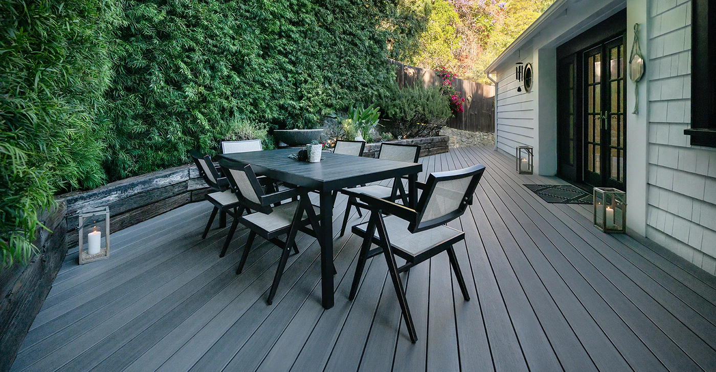 A Gray deck with variegated color visible in the boards. An outdoor dining table with sleek but casual chairs is situated in the middle of the deck.
