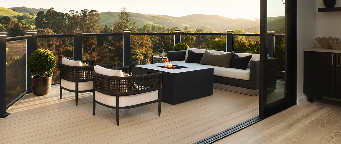 Light tan deck with a modern, outdoor fire pit that has a contained fire burning.