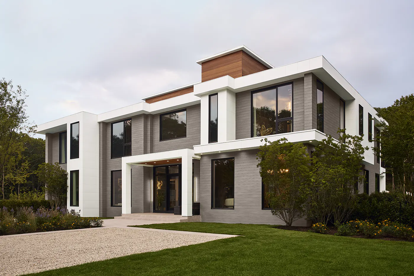 Angled view of the front of the house, the sunset reflects off of the large front windows.
