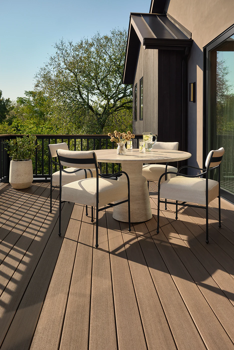 A circular table and matching white, cushioned chairs creates a sitting area close to the edge of the deck where it meets the side of the home