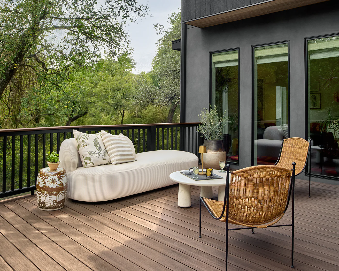 A modern, white couch and matching circular coffee table sits across from two wicker chairs on the deck