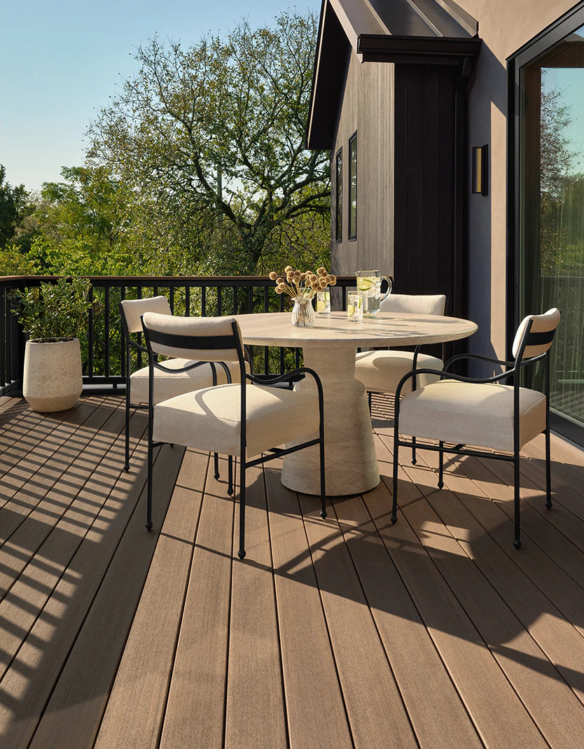 A circular table and matching white, cushioned chairs creates a sitting area close to the edge of the deck where it meets the side of the home